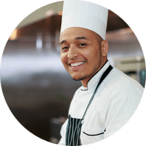 A chef with a hat and apron on in the kitchen.